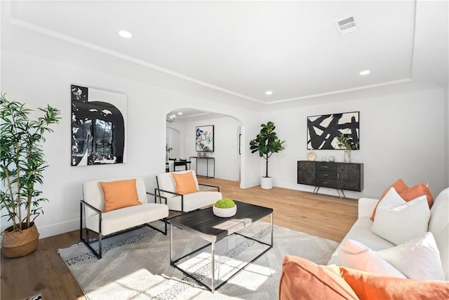 living room featuring wood finished floors, visible vents, arched walkways, and a raised ceiling