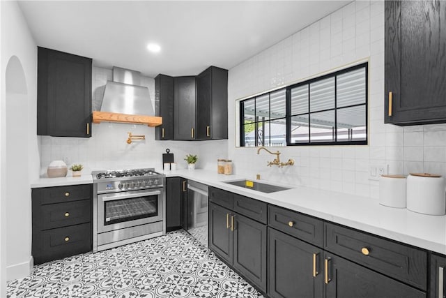 kitchen featuring stainless steel appliances, light countertops, wall chimney range hood, a sink, and decorative backsplash