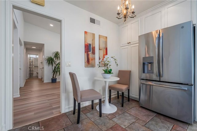 dining room featuring stone finish floor, visible vents, baseboards, and a notable chandelier