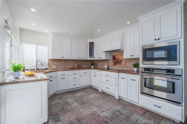 kitchen featuring a sink, tasteful backsplash, appliances with stainless steel finishes, white cabinetry, and custom range hood
