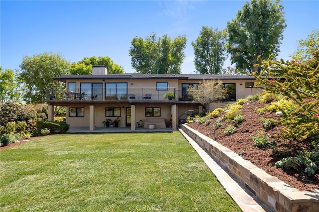 back of house with a chimney, a yard, stucco siding, a wooden deck, and a patio