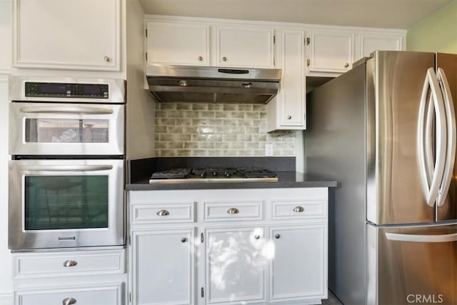 kitchen featuring white cabinets, stainless steel appliances, dark countertops, decorative backsplash, and under cabinet range hood