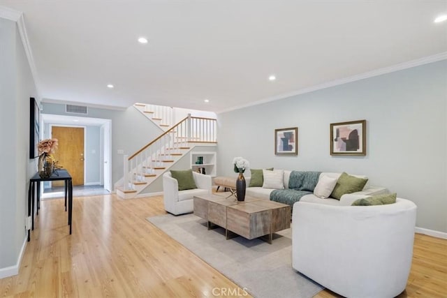 living area featuring baseboards, visible vents, light wood-style floors, stairs, and ornamental molding