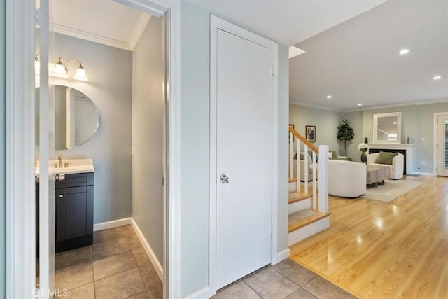 hallway featuring recessed lighting, a sink, light tile patterned flooring, crown molding, and stairs
