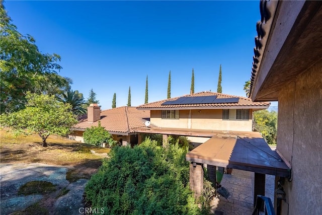 exterior space with stucco siding, a chimney, solar panels, and a tile roof