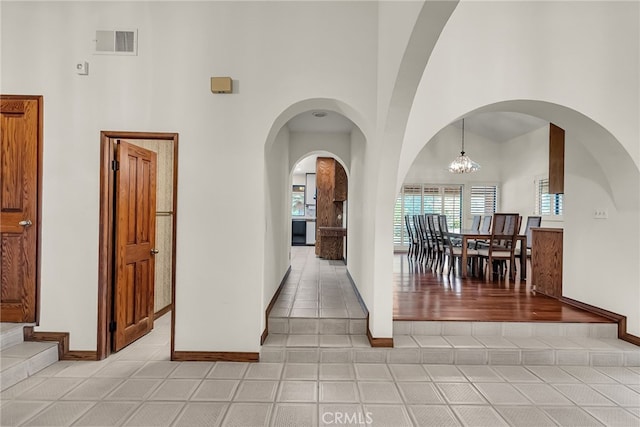 hall featuring a notable chandelier, baseboards, visible vents, and a towering ceiling