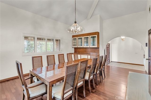 dining area featuring an inviting chandelier, arched walkways, beam ceiling, and light wood-style flooring