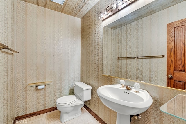 half bath featuring a sink, wallpapered walls, and toilet