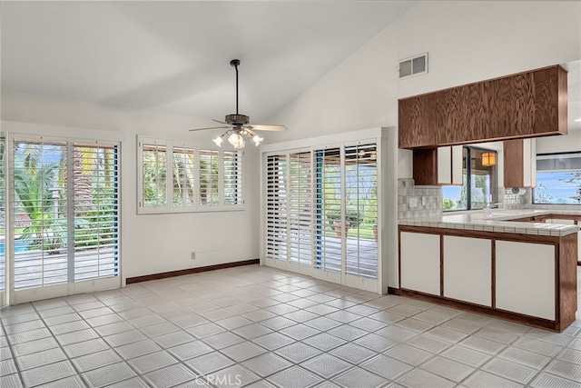 interior space featuring visible vents, decorative backsplash, baseboards, high vaulted ceiling, and a ceiling fan