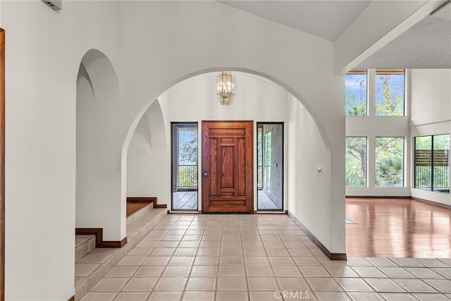 foyer with light tile patterned flooring, a high ceiling, a chandelier, and baseboards