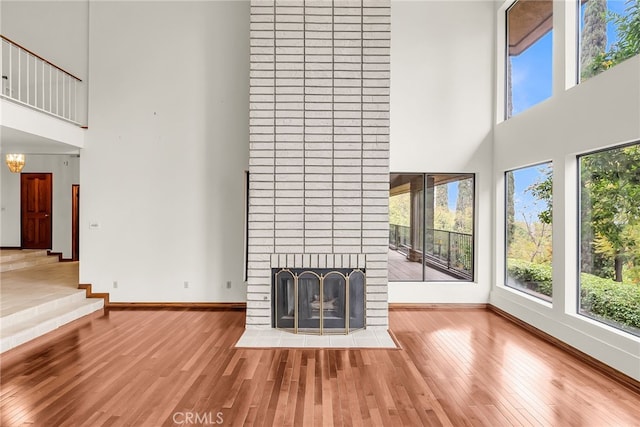 unfurnished living room featuring baseboards, a wealth of natural light, wood finished floors, and a towering ceiling