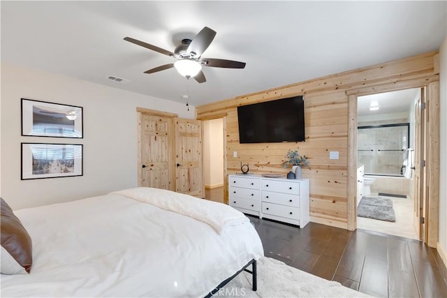 bedroom featuring dark wood-style floors, a ceiling fan, wood walls, ensuite bath, and visible vents