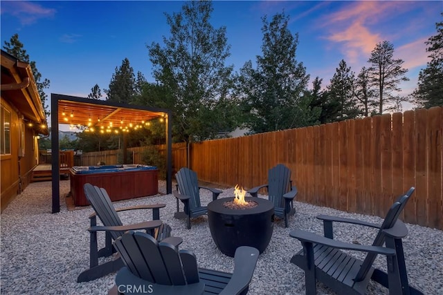 patio terrace at dusk featuring a fenced backyard, a wooden deck, an outdoor fire pit, and a hot tub