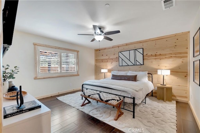 bedroom featuring wood walls, wood finished floors, visible vents, a ceiling fan, and baseboards