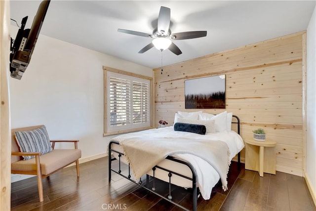 bedroom featuring a ceiling fan, baseboards, dark wood-style flooring, and wooden walls