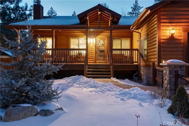 snow covered property featuring faux log siding, a porch, and a chimney