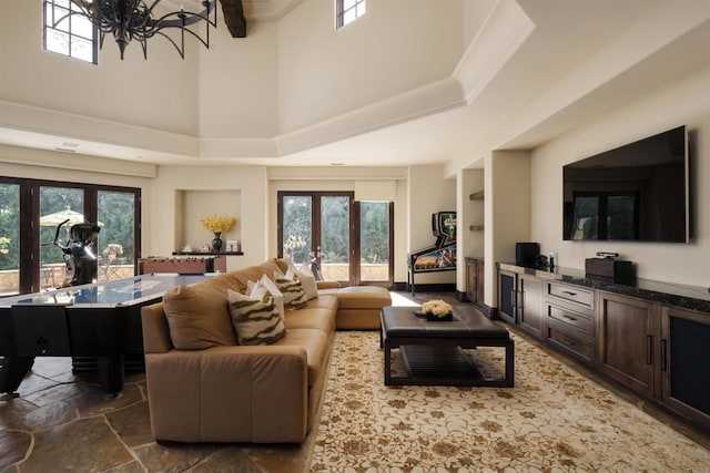 living area featuring french doors, a high ceiling, stone finish floor, and a notable chandelier
