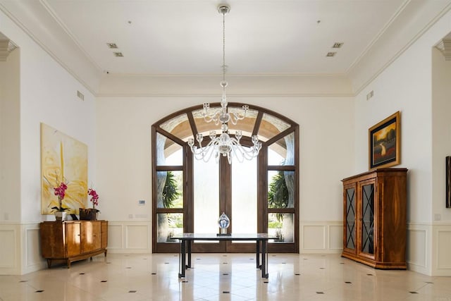entrance foyer with light tile patterned flooring, a decorative wall, wainscoting, and an inviting chandelier