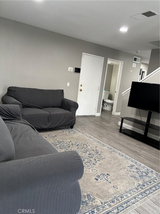 living area featuring baseboards, wood finished floors, visible vents, and stairs
