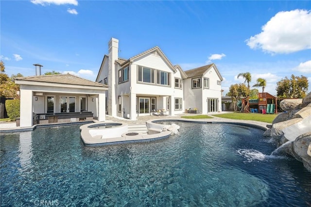 rear view of property featuring a chimney, an outdoor pool, a patio, and an in ground hot tub