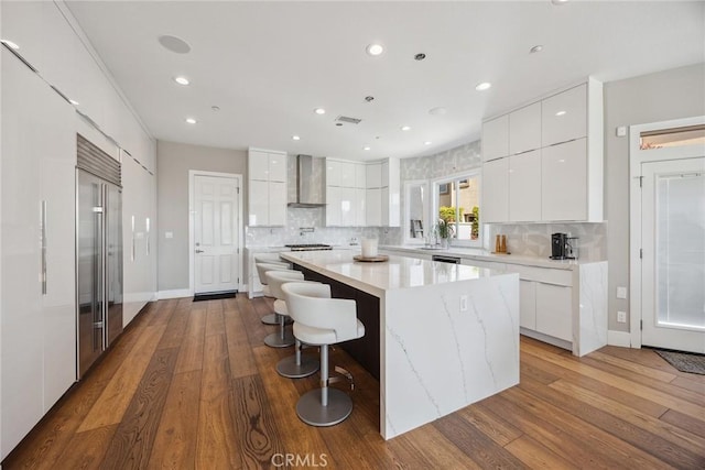 kitchen with wood finished floors, backsplash, modern cabinets, and wall chimney range hood