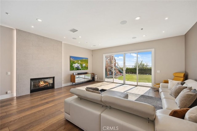 living room featuring recessed lighting, a tiled fireplace, visible vents, baseboards, and wood finished floors