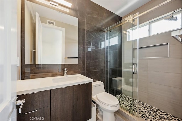full bath featuring visible vents, a stall shower, toilet, tile walls, and vanity