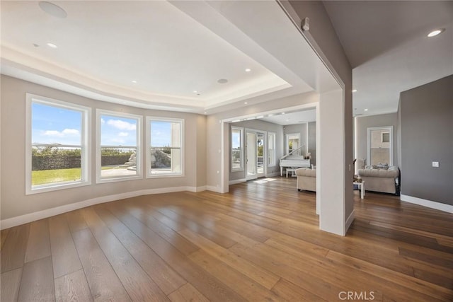 unfurnished living room featuring a healthy amount of sunlight, a tray ceiling, wood-type flooring, and baseboards
