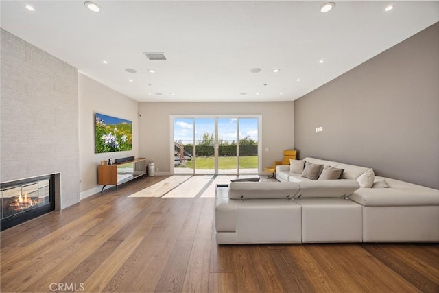 living area with recessed lighting, a large fireplace, visible vents, and wood finished floors