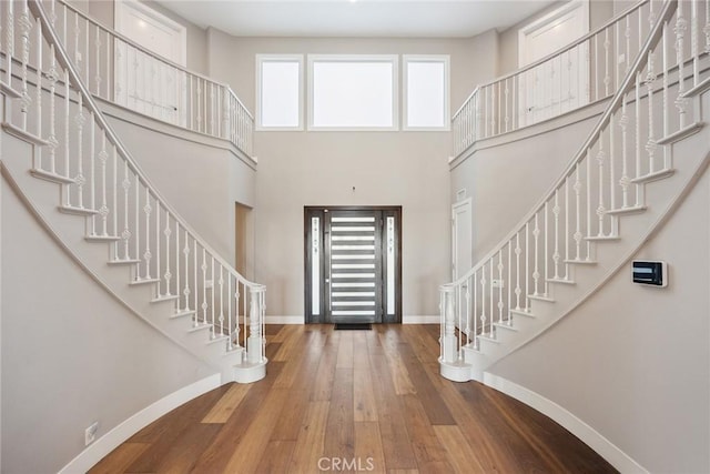 foyer entrance with a towering ceiling, hardwood / wood-style floors, stairs, and baseboards