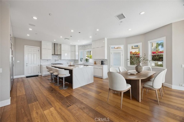 kitchen with tasteful backsplash, light countertops, wall chimney range hood, white cabinetry, and a center island