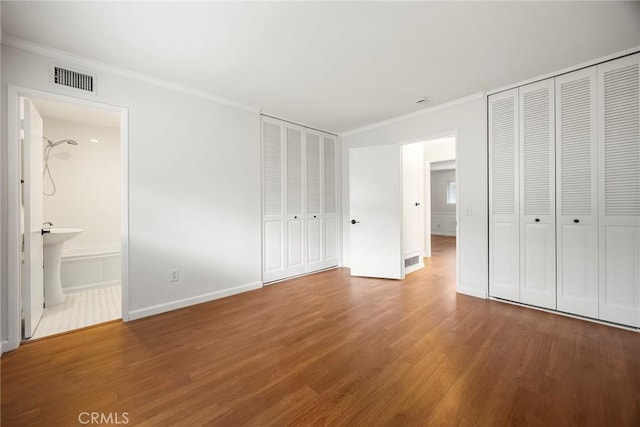 unfurnished bedroom featuring wood finished floors, multiple closets, baseboards, ornamental molding, and visible vents