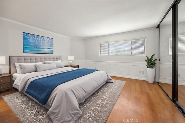 bedroom with crown molding, a wainscoted wall, and light wood finished floors
