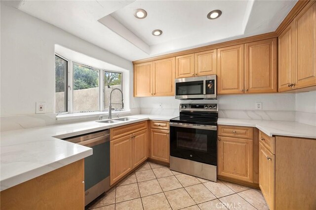 kitchen with a sink, light tile patterned floors, stainless steel appliances, a raised ceiling, and recessed lighting
