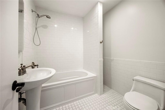 full bathroom with tile walls, toilet, a wainscoted wall, and shower / washtub combination