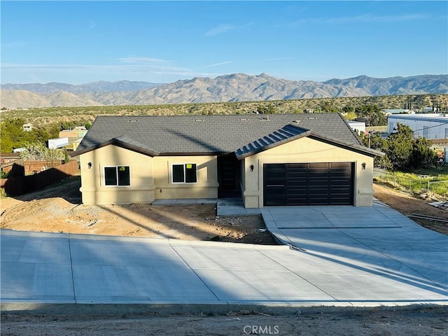 single story home with a garage, a mountain view, stucco siding, and driveway