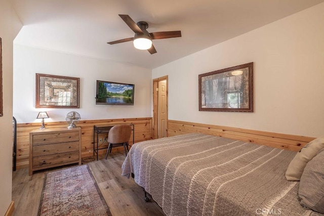bedroom featuring a wainscoted wall, wood finished floors, wooden walls, and ceiling fan
