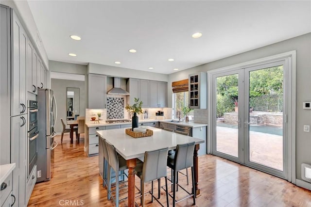 kitchen with a breakfast bar area, wall chimney range hood, light wood-type flooring, a sink, and backsplash