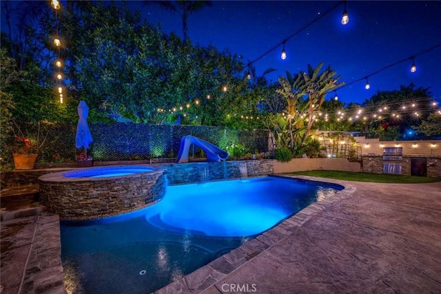 pool at twilight with an outdoor kitchen, a pool with connected hot tub, a water slide, and a fenced backyard
