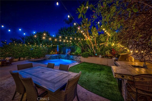 patio at night with a fenced in pool, a fenced backyard, and outdoor dining space