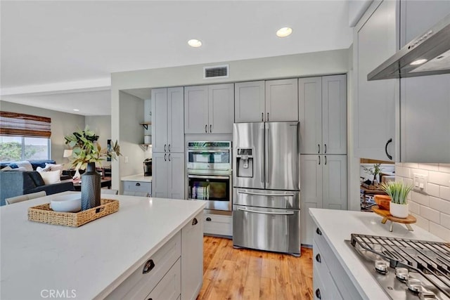 kitchen with visible vents, decorative backsplash, light countertops, appliances with stainless steel finishes, and exhaust hood