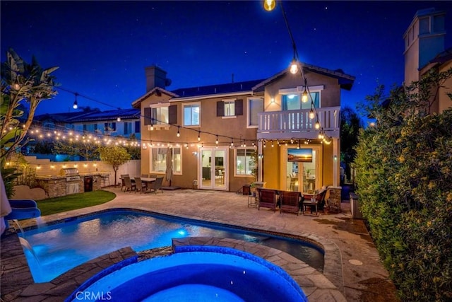 back of house at night with area for grilling, solar panels, a balcony, french doors, and a patio