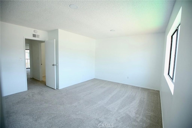 empty room with visible vents, a textured ceiling, and light colored carpet