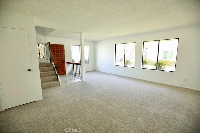unfurnished living room with light carpet, a textured ceiling, and stairway