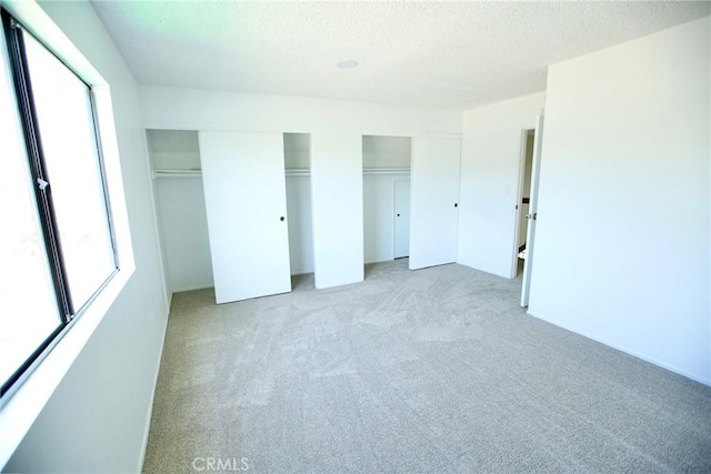 unfurnished bedroom with multiple closets, a textured ceiling, and light colored carpet