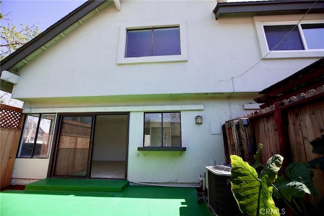 back of house with fence, central AC unit, and stucco siding