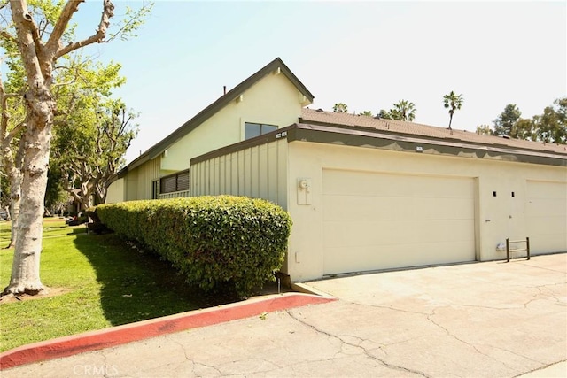 view of side of home featuring stucco siding, a lawn, driveway, and a garage