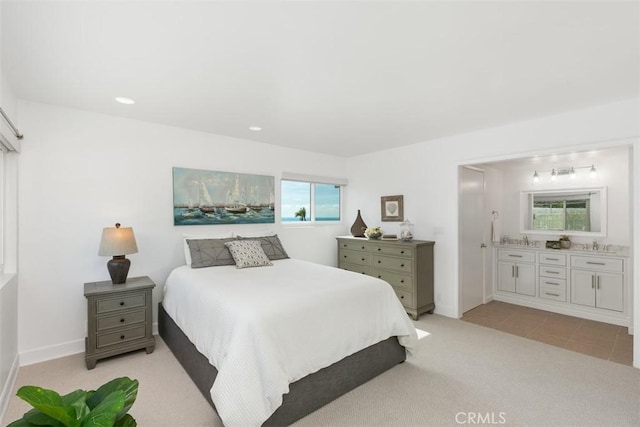 bedroom featuring light colored carpet, ensuite bath, multiple windows, and a sink