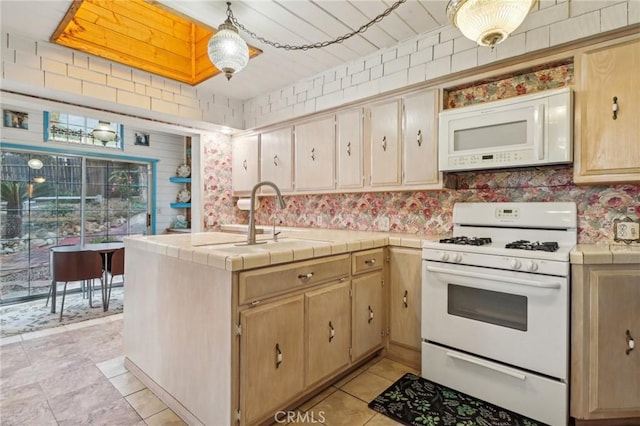 kitchen with a peninsula, a sink, white appliances, tile counters, and hanging light fixtures