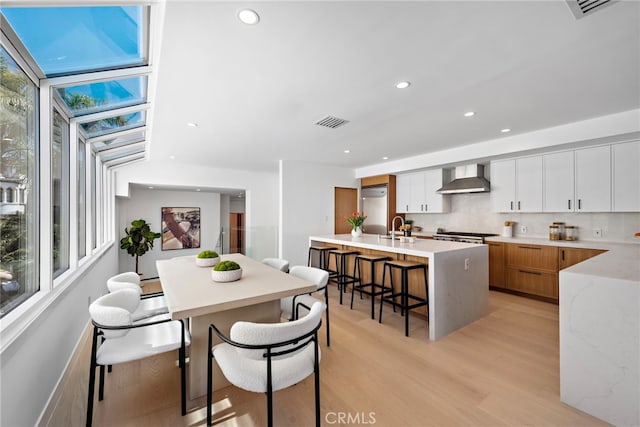 309 Carnation Ave Unit 4, Corona Del Mar, CA 92625 - kitchen featuring wall chimney range hood, refrigerator, a center island with sink, light wood-style flooring, and a kitchen breakfast bar
